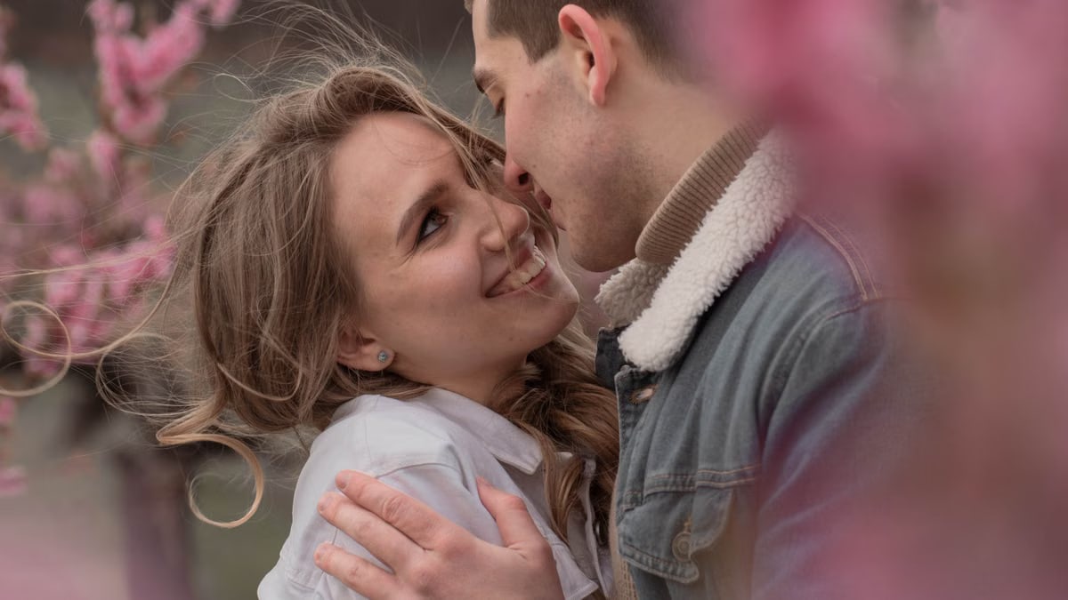 Happy couple embracing in a field with pink spring flowers, exuding love and joy.